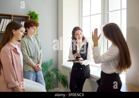 Students raising hands in engaging lesson with smiling teacher by classroom window Stock Photo
