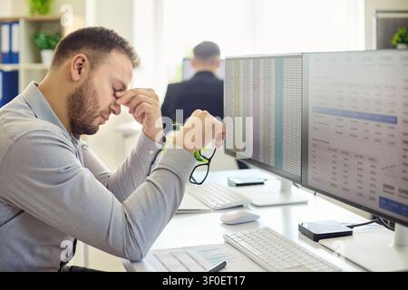 Stressed employee man at computer with spreadsheets suffering burnout fatigue Stock Photo