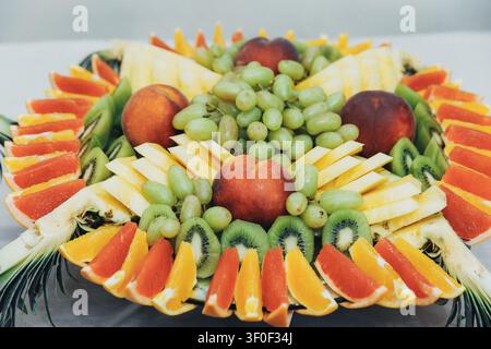 Vibrant fruit arrangement artfully displayed on a platter. Fresh grapes, peaches, kiwis, and citrus slices form a circular design. Colorful slices of Stock Photo