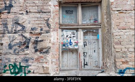 A dilapidated house facade with graffiti on the exposed bricks, featuring windows with broken panes Stock Photo