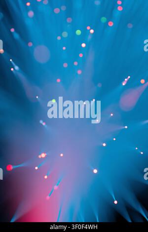 Macro photography of fiber optic strands emitting scattered light points in red, green, and pink tones against a deep teal background. The defocused b Stock Photo