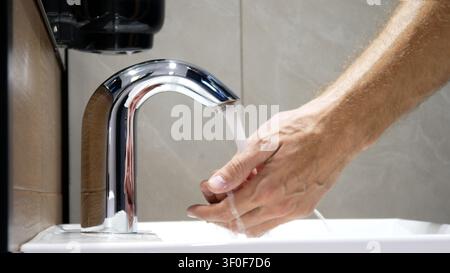 A man washes his hands using a touchless faucet close-up Stock Photo