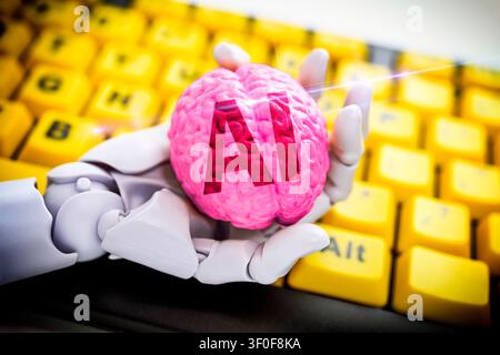 Robot hand holding a brain labeled AI in front of a computer keyboard, symbolic photo artificial intelligence, photomontage Stock Photo