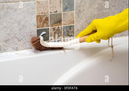Hand in yellow glove cleaning bathroom wall with brush Stock Photo