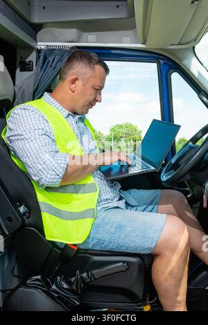 Vertical view of a delivery worker in safety vest using computer inside commercial van Stock Photo