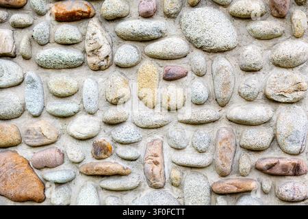 Rounded Pebble Stone Wall Texture. Rounded pebbles set in mortar form a textured stone wall with gray, beige, and brown natural rock patterns. Stock Photo