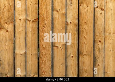 Vertical Wooden Plank Fence Texture. Vertical wooden planks form a warm rustic fence texture with visible knots, grain, seams, and golden brown boards Stock Photo