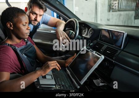 Two mechanics are using diagnostic software on a laptop to examine a car in an auto repair shop Stock Photo