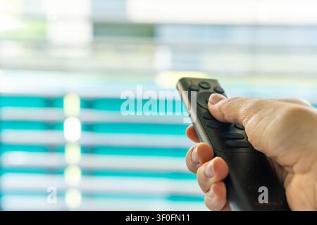 Close-up of a hand using a remote control to operate exterior window blinds. Smart home technology and automated sun protection concept. Stock Photo