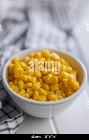 Close-up of bright yellow sweet corn kernels in a white bowl with a jar of corn in the background, suggesting fresh, simple home cooking, wholesome me Stock Photo