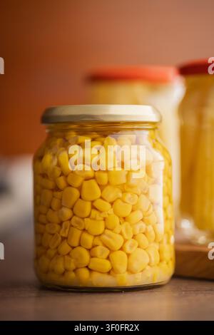 Close-up of bright yellow corn kernels preserved in a sealed glass jar on a wooden surface, evoking pantry storage, homemade canning, cooking ingredie Stock Photo
