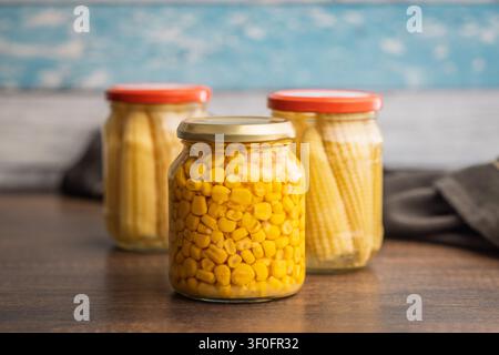 Close-up of bright yellow corn kernels preserved in a sealed glass jar on a wooden surface, evoking pantry storage, homemade canning, cooking ingredie Stock Photo