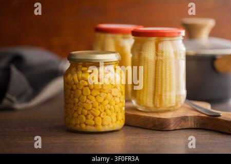 Close-up of bright yellow corn kernels preserved in a sealed glass jar on a wooden surface, evoking pantry storage, homemade canning, cooking ingredie Stock Photo
