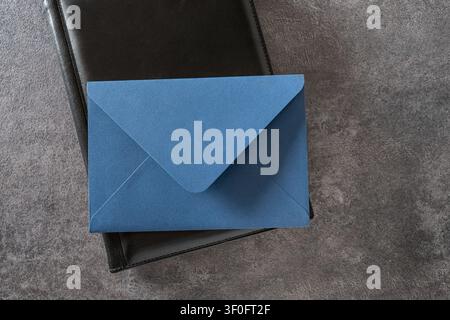 Blue paper envelope placed on a black notebook over gray textured background with copy space. Top view. Stock Photo