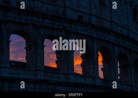 Colosseum (Amphitheatrum Flavium) arches in dark silhouette against a fiery orange sunset sky. Rome, Italy. Stock Photo