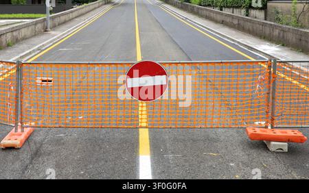 No entry traffic sign on temporary safety orange plastic netting fence, with a closed empty two lane road on behind it. Background for copy space Stock Photo
