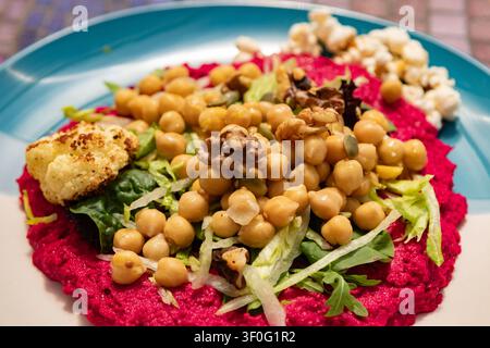 Chickpea salad and toasted walnuts on a bed of luscious beetroot hummus, with baked cauliflower, popcorn and a scattering of sunflower seeds, close up Stock Photo