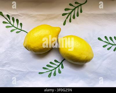 Leander, Texas, USA - July 6, 2026: Photo of two fresh lemons resting on a simple green and white tablecloth with a leaf design. Stock Photo
