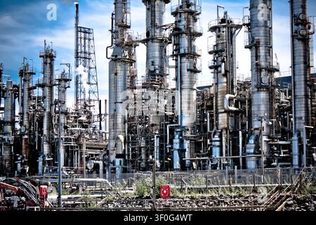 Workers manage operations at a large industrial plant with tall towers and extensive piping structures during daylight hours Stock Photo