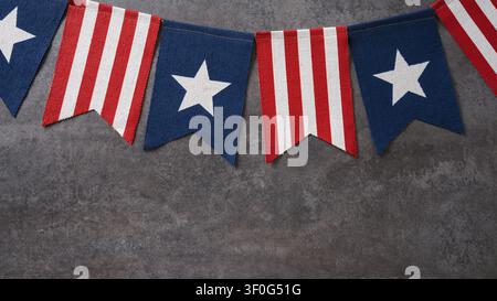 Red white and blue patriotic bunting hanging over gray textured background with copy space. Top view. Banner Stock Photo