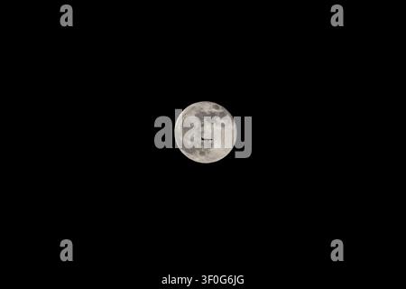 The silhouette of a large passenger plane against the full moon in the night sky. A serendipitous, perfect moment captured in high-contrast black and Stock Photo