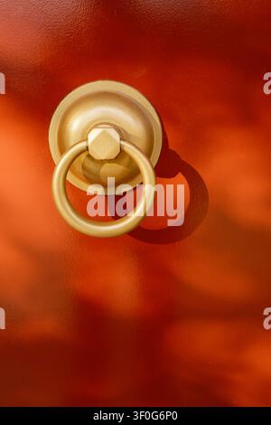 Macro portrait framing of a heavy gold brass ring door knocker on a bright red wooden gate panel, Osaka, Japan Stock Photo