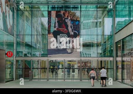 Glass entrance to the Bullring shopping centre featuring a large billboard and Selfridges sign, Birmingham, UK Stock Photo