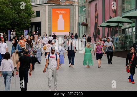 Crowd of pedestrians walking past a billboard outside the Bullring shopping centre in Birmingham, UK Stock Photo