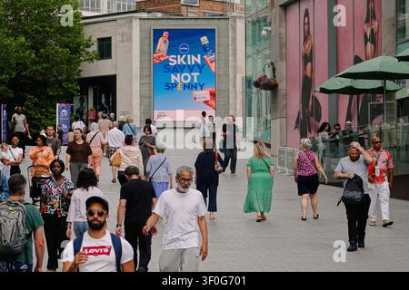 Crowd of pedestrians walking past a billboard outside the Bullring shopping centre in Birmingham, UK Stock Photo