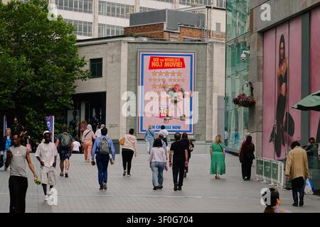 Crowd of pedestrians walking past a billboard outside the Bullring shopping centre in Birmingham, UK Stock Photo