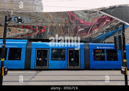 West Midlands Metro tram passing the reflective facade of Birmingham New Street station, UK Stock Photo