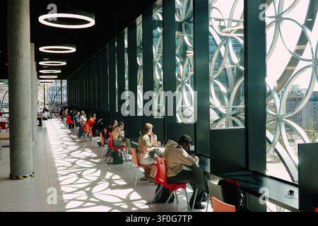 Students studying by large windows with patterned shadows inside the Library of Birmingham, UK Stock Photo
