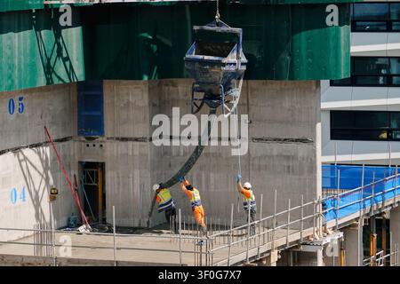 Construction workers pouring concrete using a crane skip on a high-rise building site in Birmingham city centre, UK Stock Photo