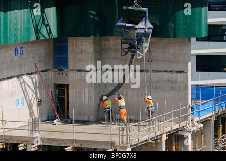 Construction workers pouring concrete using a crane skip on a high-rise building site in Birmingham city centre, UK Stock Photo