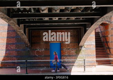 A woman with a shopping trolley walking under the Brewmasters Bridge in Birmingham canal network, UK Stock Photo