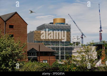 View across rooftops towards the iconic Library of Birmingham and construction cranes under a cloudy sky, UK Stock Photo