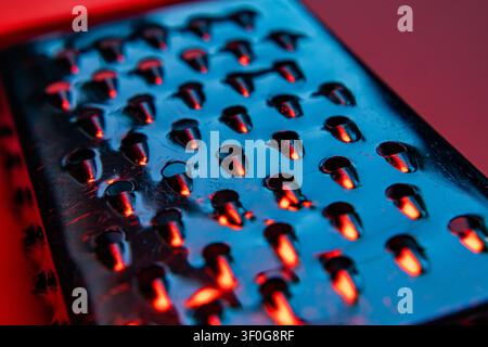 Cheese grater surface with raised holes glowing red and blue in abstract close up Stock Photo