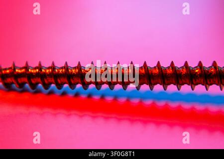 Screw threading stretched horizontally with reflection against vivid pink and blue backdrop Stock Photo