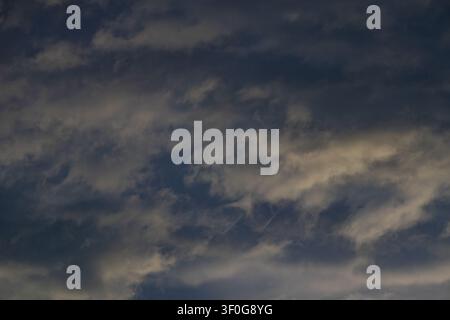Layered clouds streaking across dark blue sky with faint bands of pale light Stock Photo