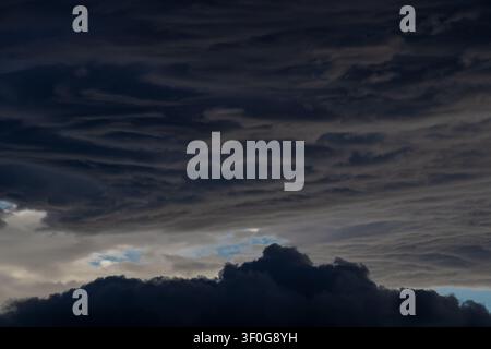 Dark storm clouds layered across sky with small patches of blue breaking through Stock Photo