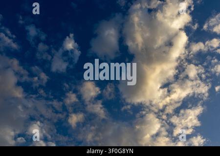 Scattered clouds catching golden light against deep blue sky in layered tones Stock Photo