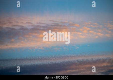 Blue sky streaked with pink and gold clouds catching sunset light in layered bands Stock Photo