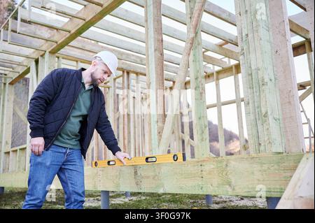 Builder checks horizontal alignment of timber beam with spirit level at construction site, concept of precision work, structural accuracy, quality control and reliable house building process Stock Photo