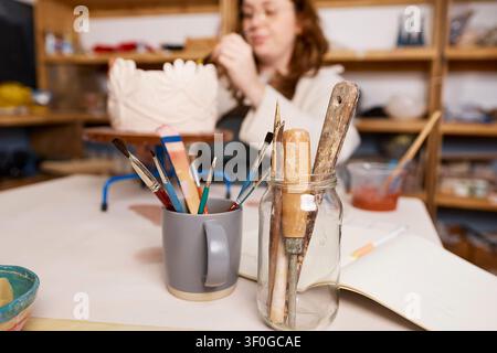 Pottery Studio Artist Working on Handcrafted Ceramic Vase With Brushes and Tools on Table Stock Photo