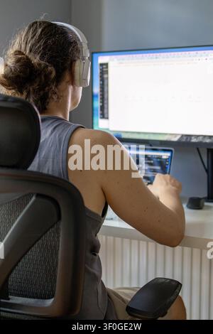 Rear view of a man working at a desk with a laptop and external monitor in a modern home office. Concept of remote work, digital profession, productiv Stock Photo