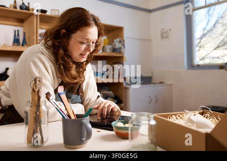Small Business Pottery Studio Owner Packing Handmade Ceramics While Using Tablet in Workshop Stock Photo