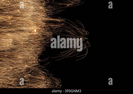 Abstract horizontal sweeps of glowing golden firework sparks with a distinct, spidery firework burst emerging on the right side against a black sky. Stock Photo