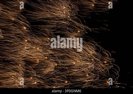 Abstract golden firework sparks sweeping in curved, wave-like light trails across a black background. Stock Photo