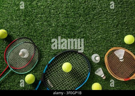 Flat lay composition with badminton rackets, tennis racket, shuttlecocks and tennis balls on artificial grass with large copy space. Stock Photo