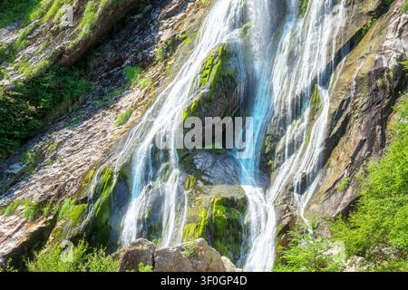 Sunny view of water flowing over rugged stone cliffs with green moss at Powerscourt waterfall in summer. Stock Photo